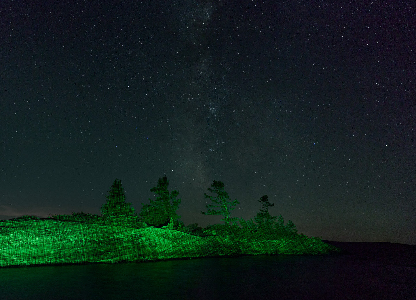 Silhouette of trees on a rocky island under a starry night sky with the Milky Way.