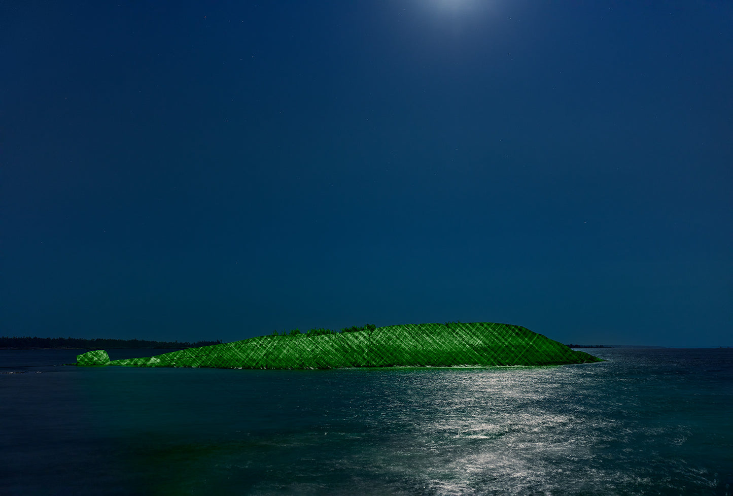 Green laser light against a rock island at night