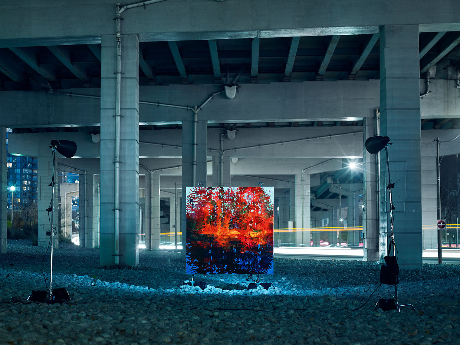 Vivid landscape painting lit beneath concrete overpass.