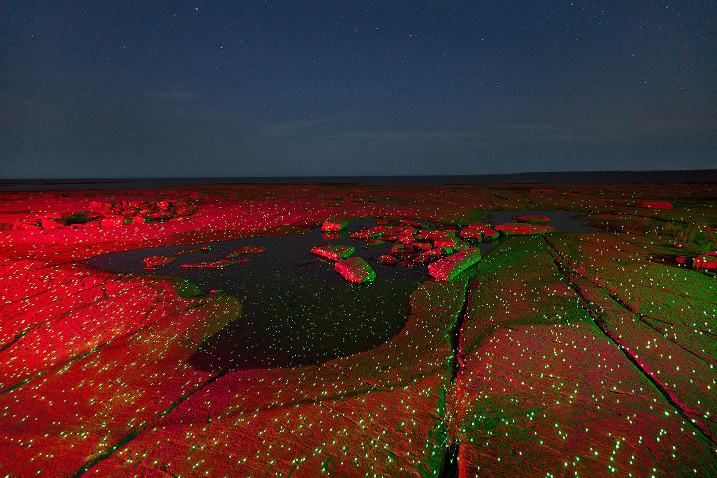 Red and green illuminated rock formation under a starry night sky