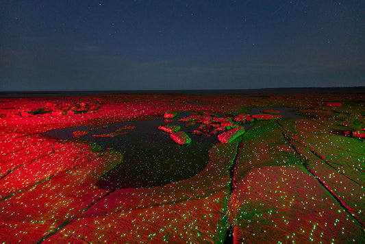 Red and green illuminated rock formation under a starry night sky