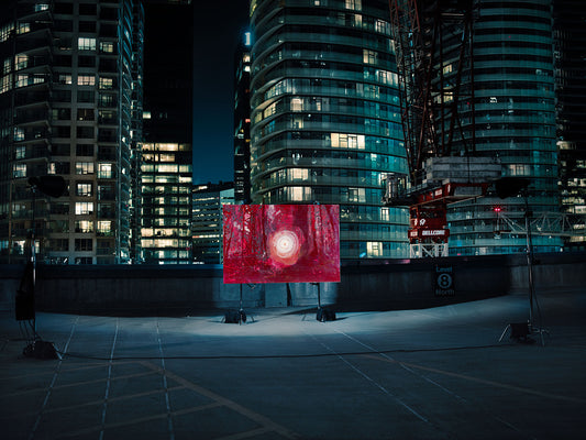 Red abstract forest painting on lit rooftop amid skyscrapers.