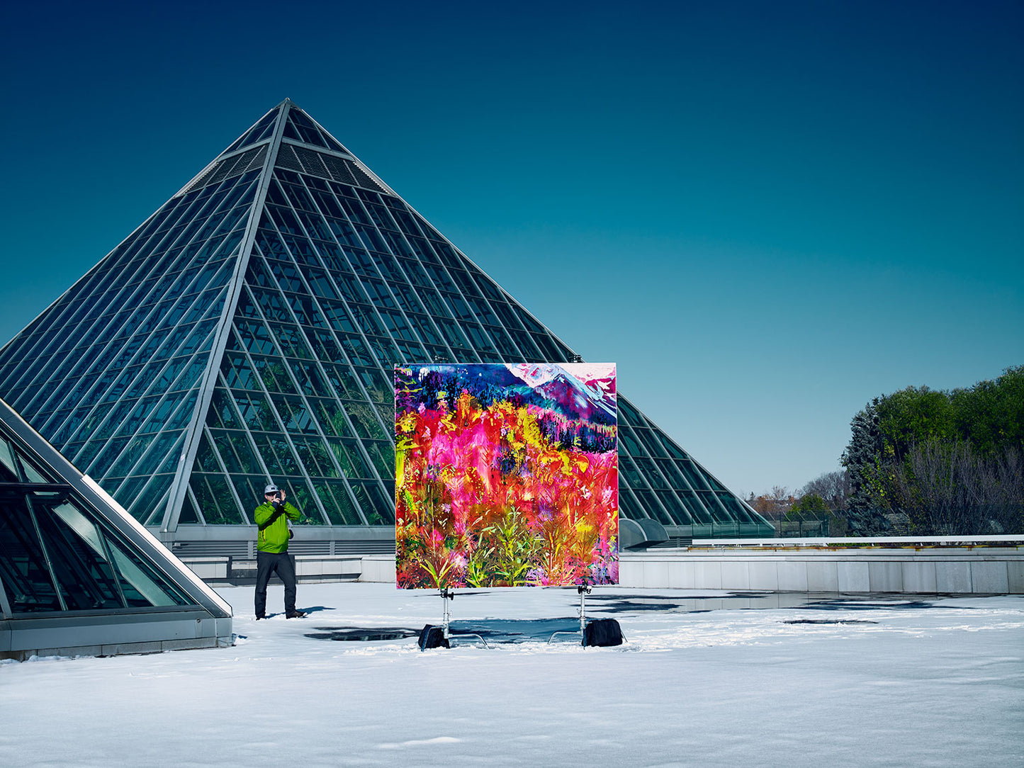 Colorful floral painting on snowy rooftop near glass pyramid.