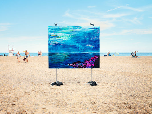 Painting on sandy beach with ocean backdrop and sunbathers.